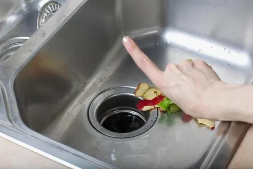 Food scraps sitting at the opening of a stainless steel kitchen sink garbage disposal