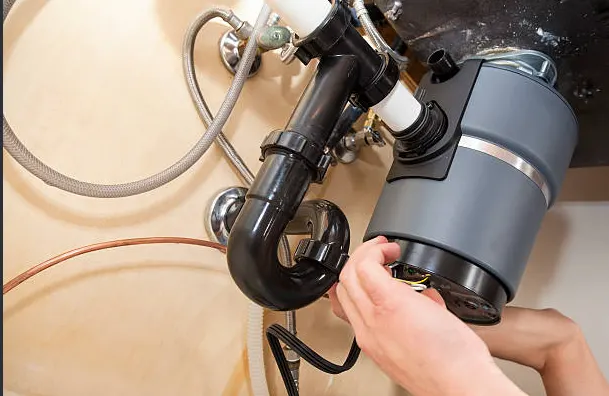 Plumber working on a garbage disposal mounted under a kitchen sink
