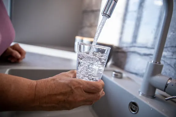 Person filling a clear glass with clean water from a modern kitchen faucet