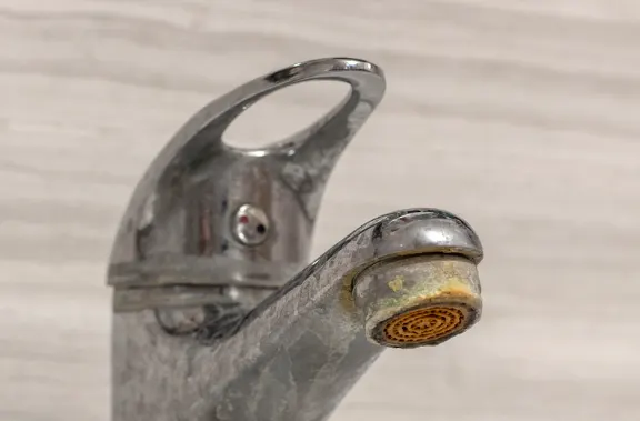 Kitchen faucet heavily coated in hard water limescale and mineral deposits