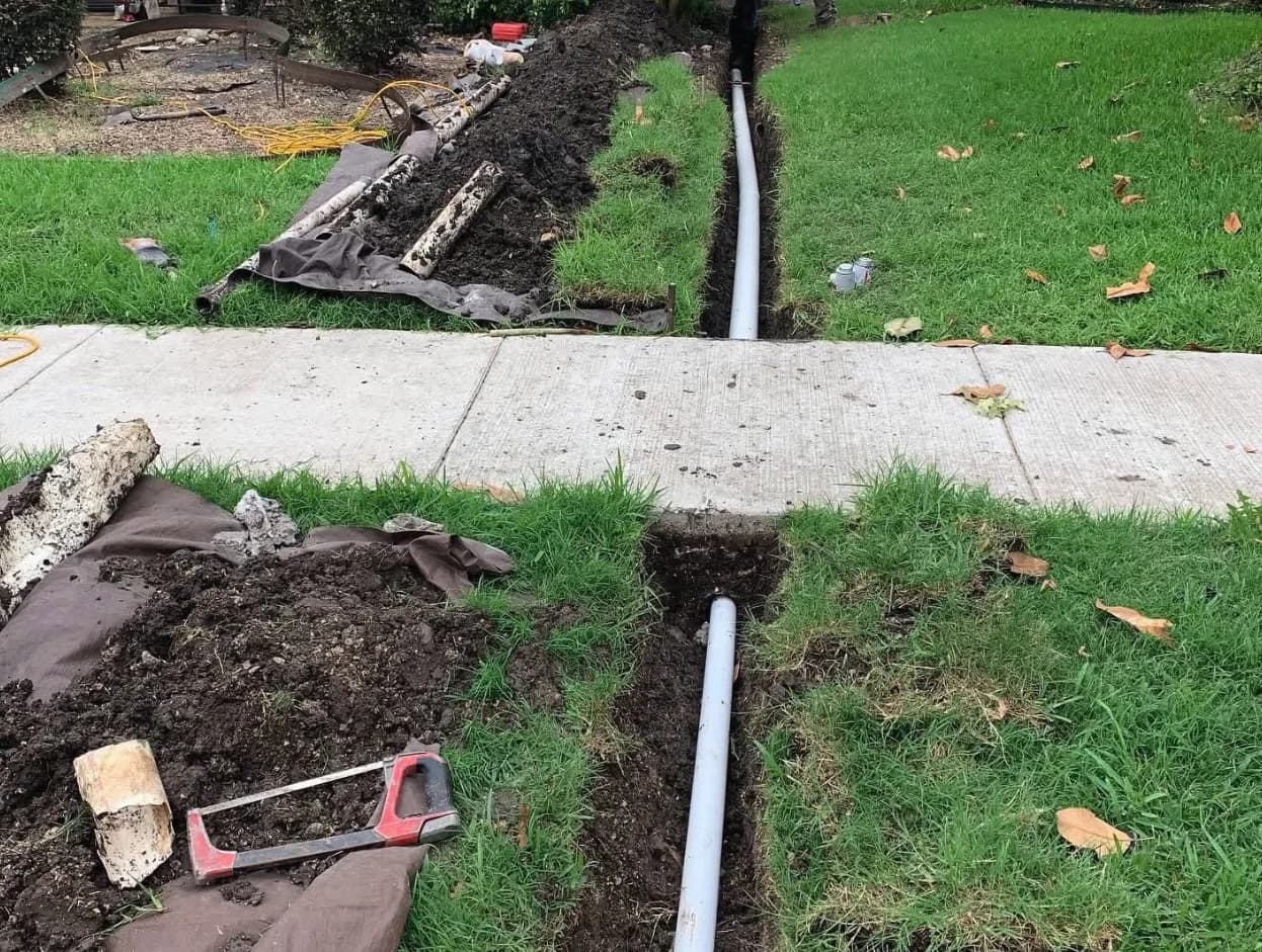 Traditional sewer line excavation trench cut through a lawn under a sidewalk