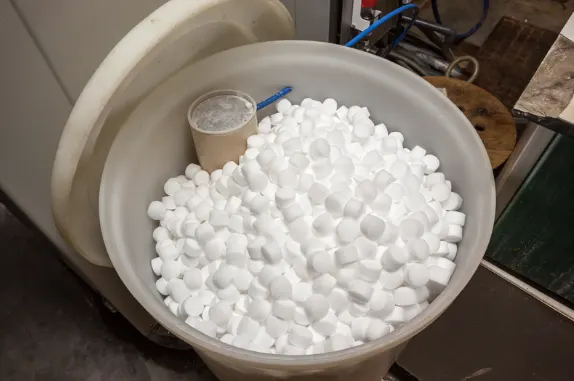 Open drum filled with white water softener salt pellets in a utility room